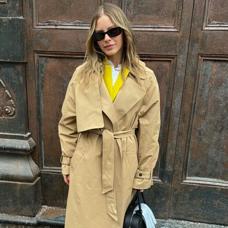 Nikki wears a trench coat with a yellow blazer.