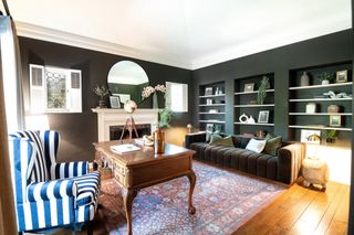 A modern study painted in a dark green with wooden desk and blue and white wingback armchair