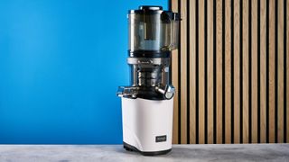 Kuvings Auto8 hands-free slow juicer photographed on a blue background.