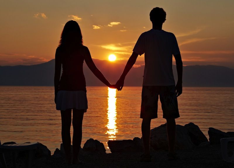 A teen couple stands watching a sunset