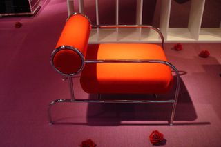 A metal structured chair with a red cushion square base and a red cylinder back.