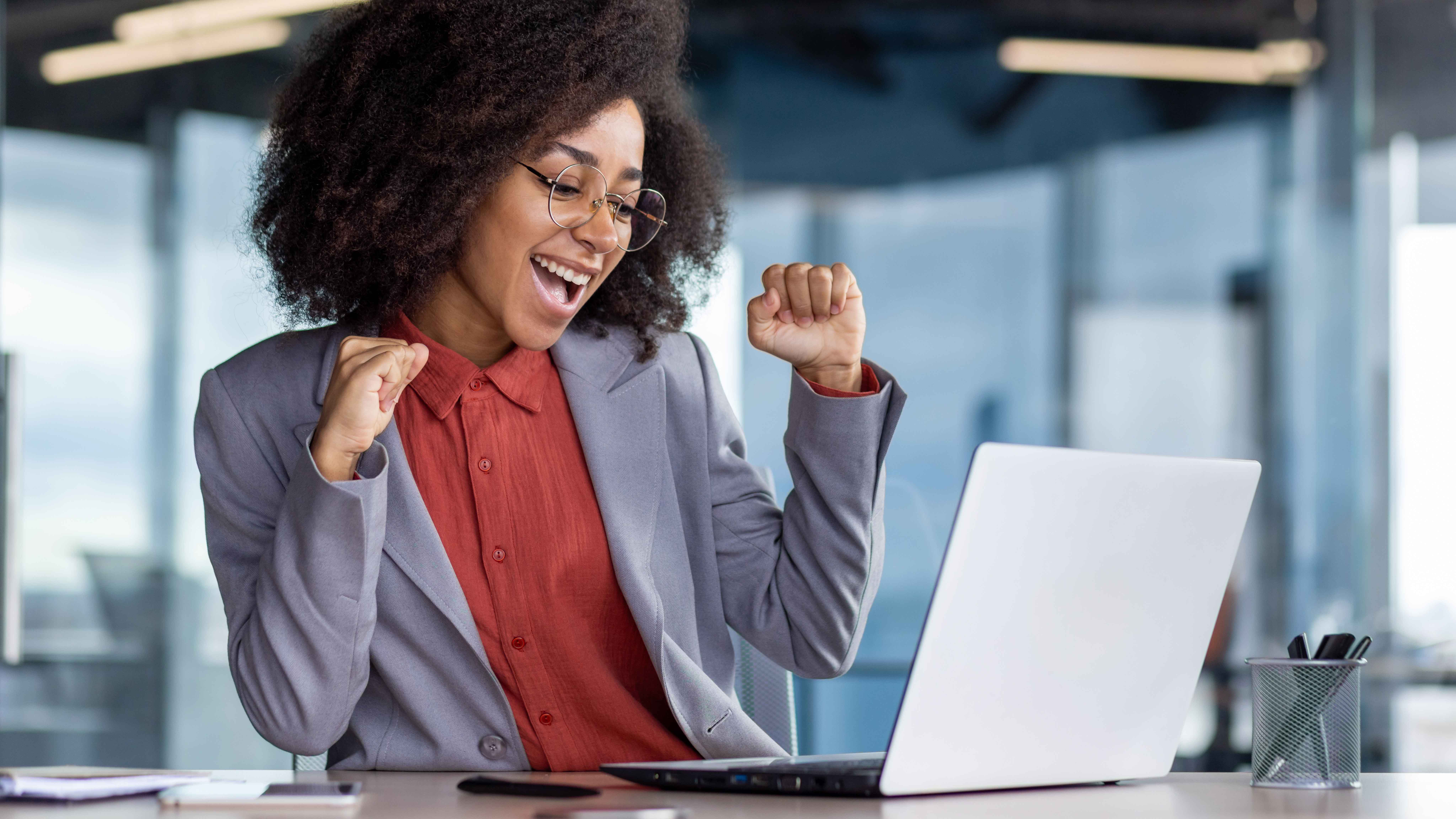 female worker with laptop celebrating in an office