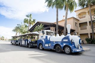 A photograph of the little blue and white train at Wyndham Residences, Costa Del Sol, which takes guests around the resort. It is parked outside reception next to some palm trees