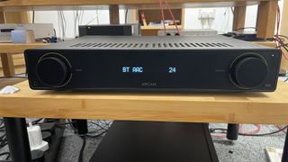 A black Arcam A5 stereo amplifier on a wooden rack