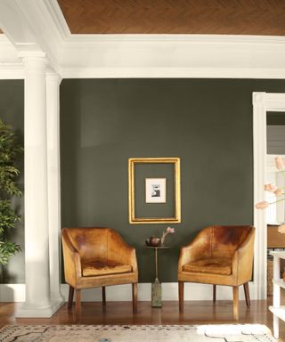 entryway with pair of tan armchairs, dark green wall with white trim and wooden floors