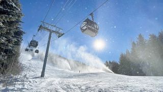 Scenic view of a ski slope with gondolas riding under a blue sky and snow guns blasting powdery goodness