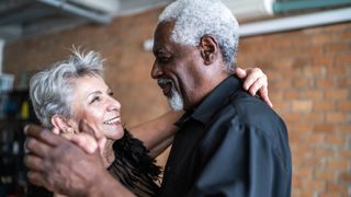 A senior couple, both with gray hair, are dancing a waltz in a dance hall.