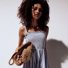 model wears striped blue and white dress and is holding a raffia tote