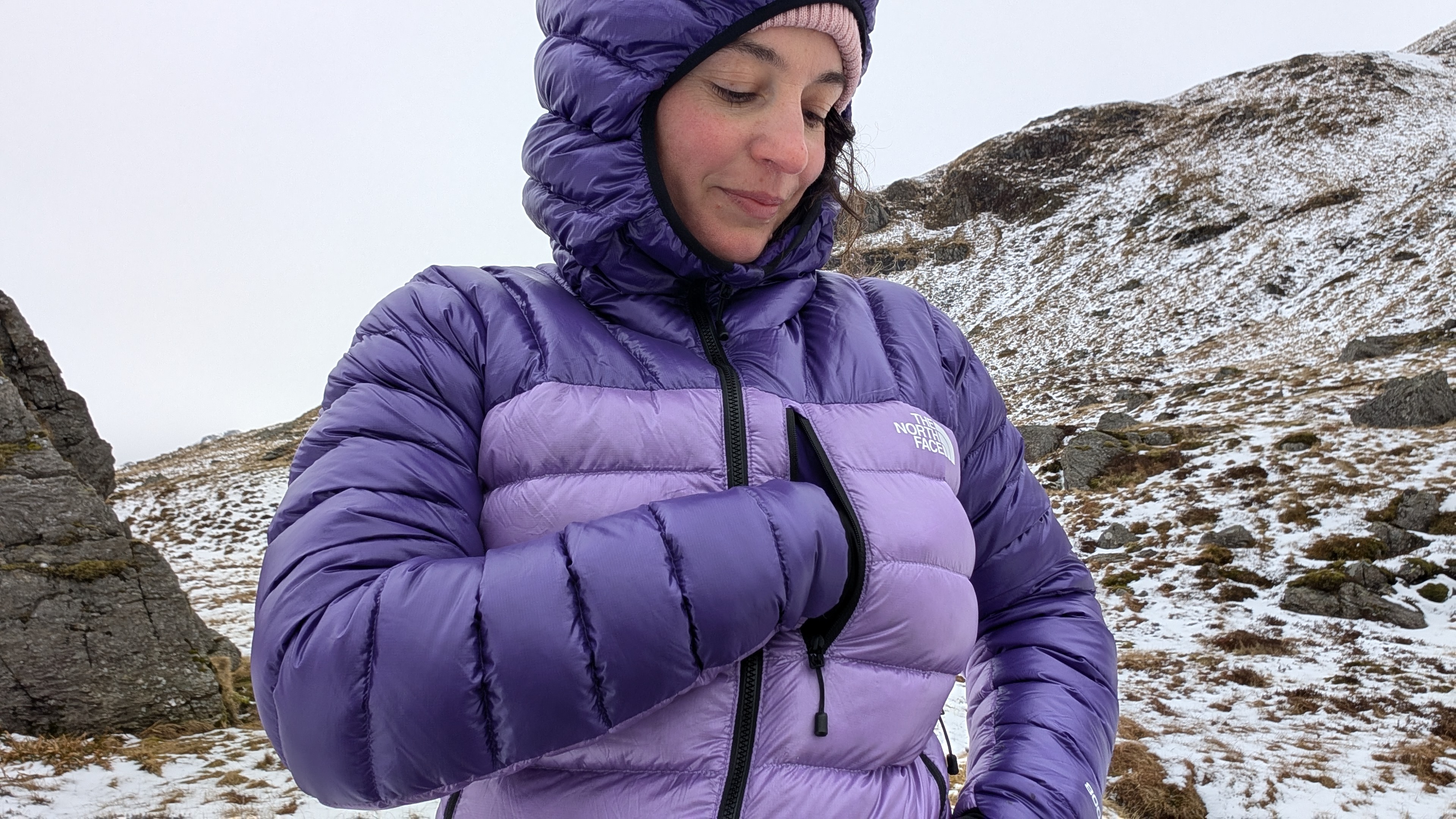 A woman hiker putting something in the chest pocket of her purple North Face Summit Breithorn Down Jacket