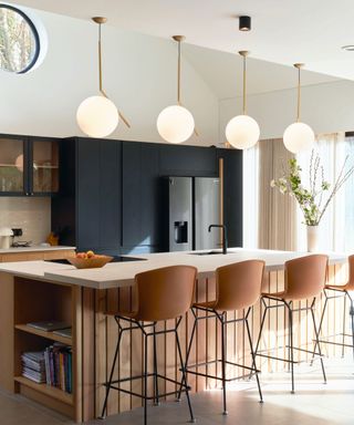 Tiered kitchen island, white countertop, wooden base, bar seating, round ceiling lights suspended above
