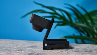 a black small 4K webcam with a red button photographed on a beige surface against a blue background