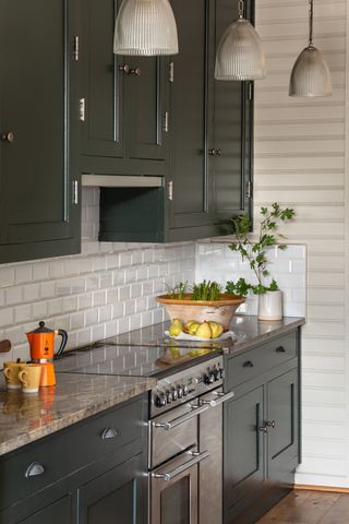 A dark green kitchen with white tiles and a triple run of pendants