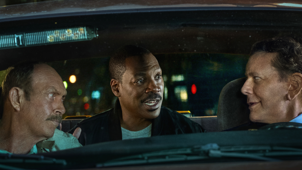 John Ashton and Judge Reinhold talk in front of the patrol car while Eddie Murphy sits and talks in the back seat in Beverly Hills Cop: Axel F.