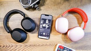 Hero image for best best wireless headphones showing Sony WH-1000XM5 and. AirPods Max placed either side of an iPhone