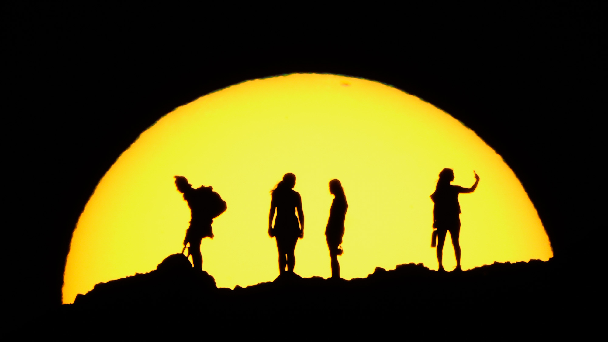 People are silhouetted against the setting sun while hiking in the mountains in Phoenix, USA