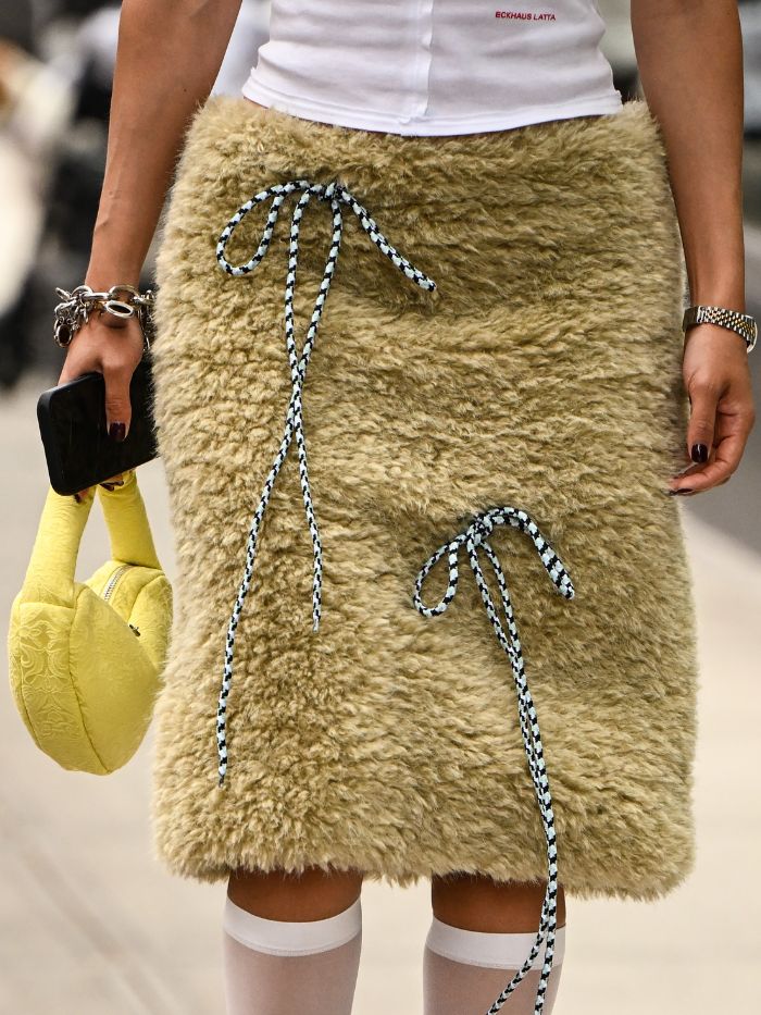 A woman at New York Fashion Week wearing a fluffy yellow skirt with a black manicure