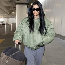 Amelia gray wears sunglasses, gray sweatpants, and a green puffer jacket.