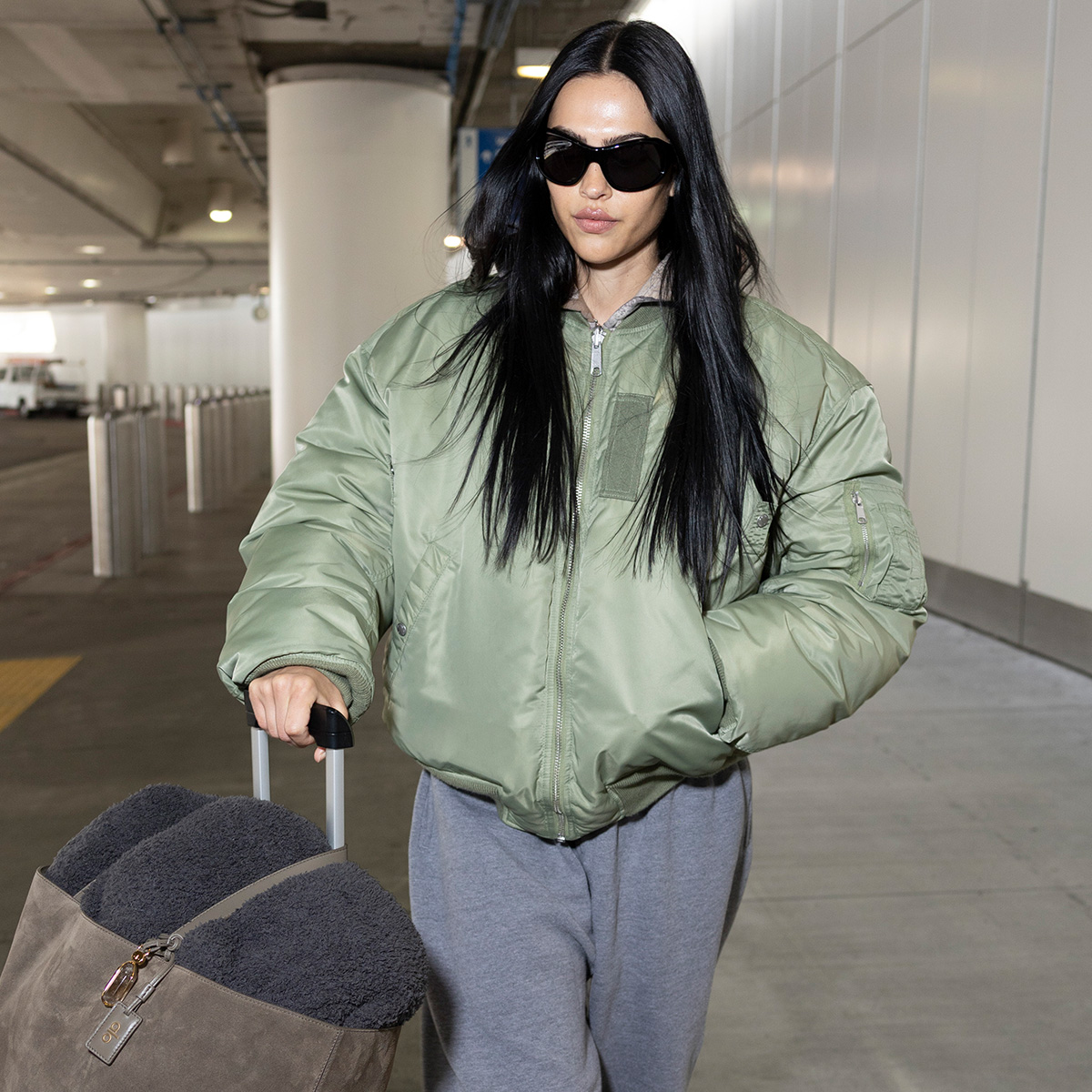 Amelia gray wears sunglasses, gray sweatpants, and a green puffer jacket.