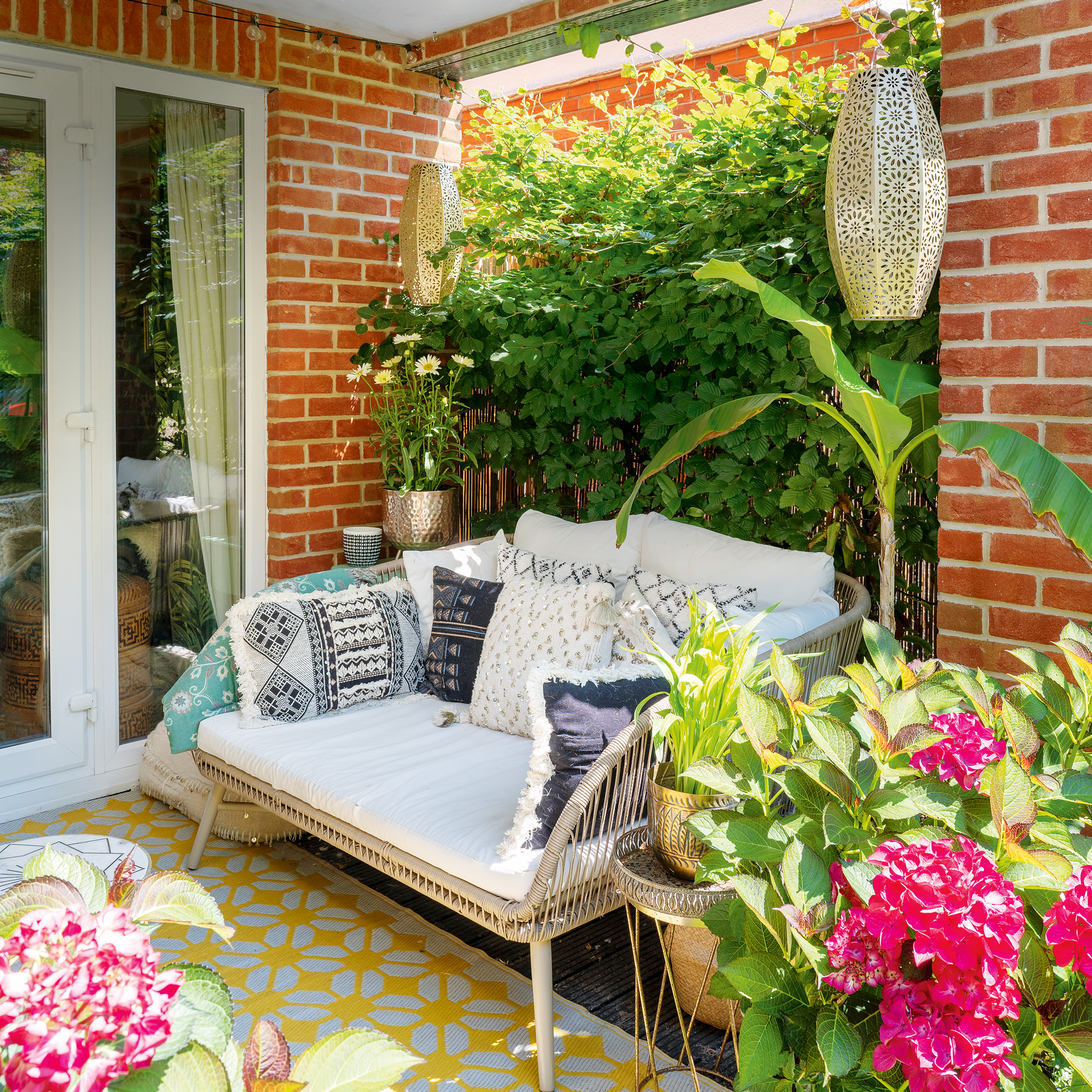 a small patio area with a two seater outdoor sofa and potted hydrangeas