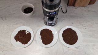 Three plates of coffee grounds in front of the KitchenAid Coffee Grinder