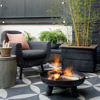 Garden terrace area, with patterned paving, firepit and outdoor lighting, bamboo and foliage plants, garden chair and table