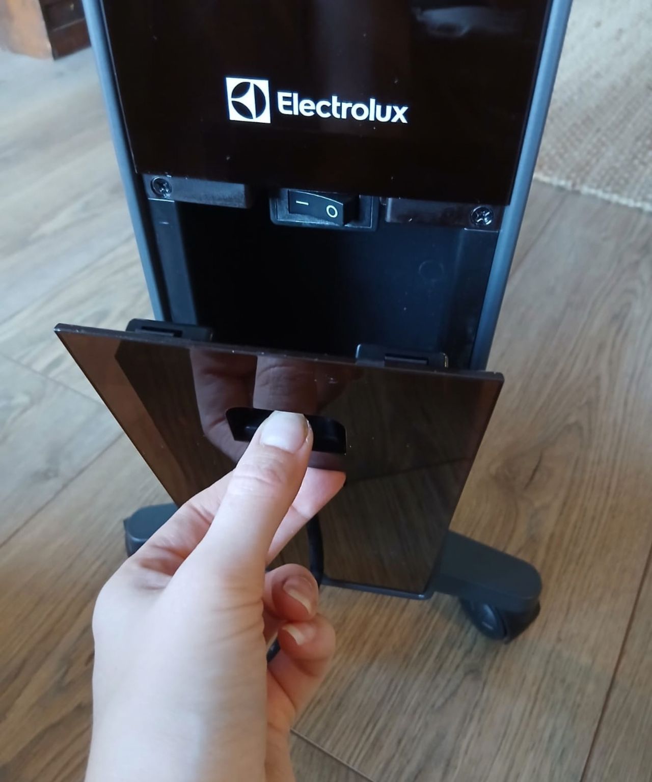 Hand opening the hinged cover on the heater's base, revealing the power switch below the Electrolux logo.
