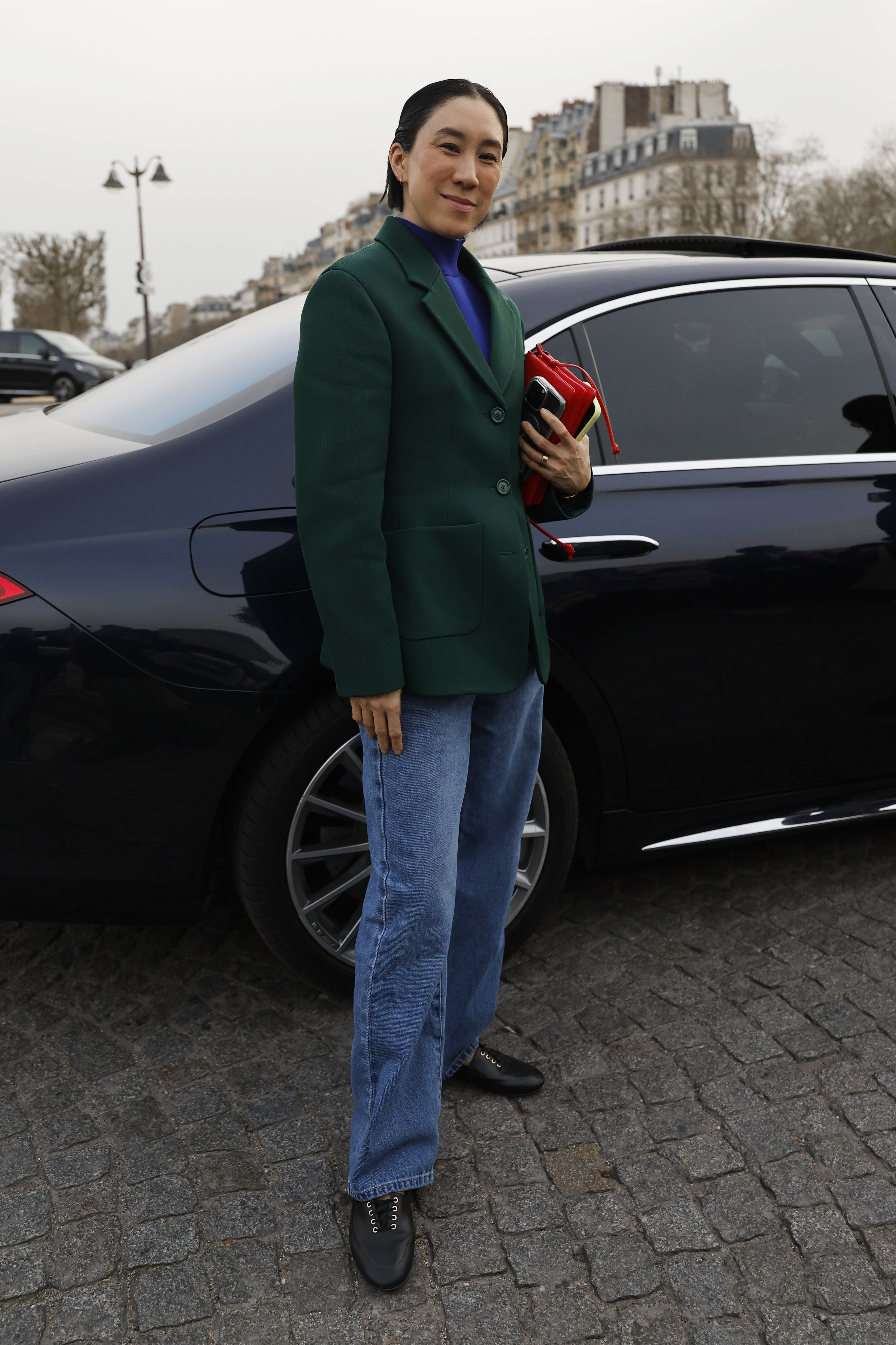 Eva Chen wears blue turtleneck top, green blazer, blue jeans, black derby shoes, red bag, outside Givenchy Fall/Winter 2026 runway on March 06, 2026 in Paris, France.