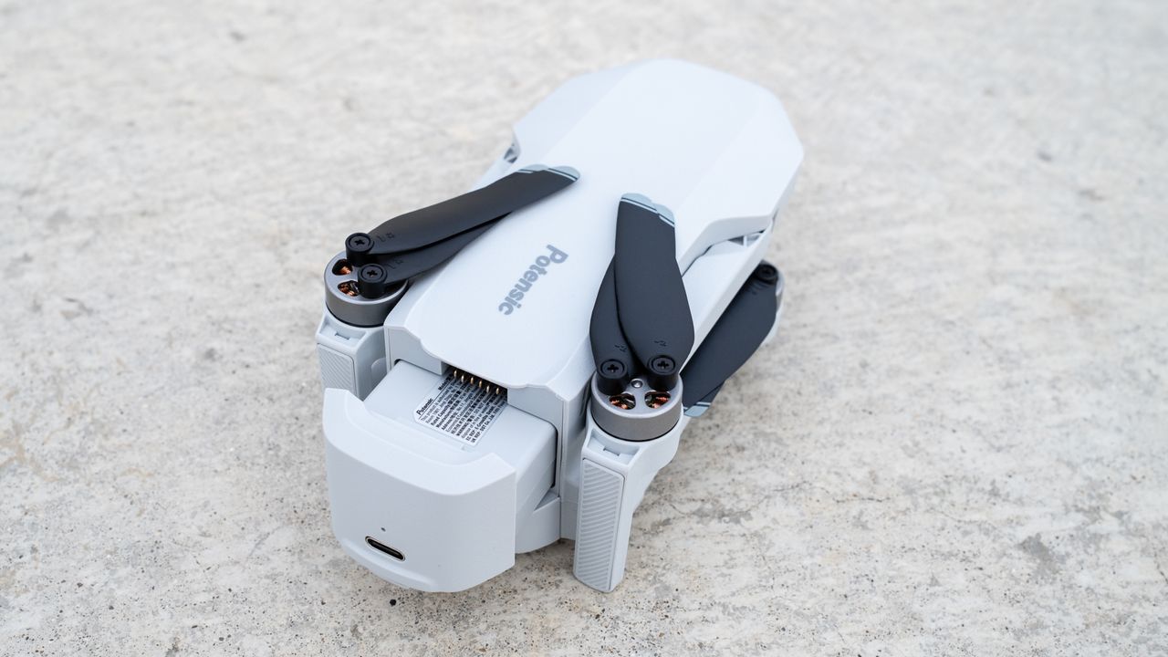 a white folded drone with black copter blades sits on a stone surface.