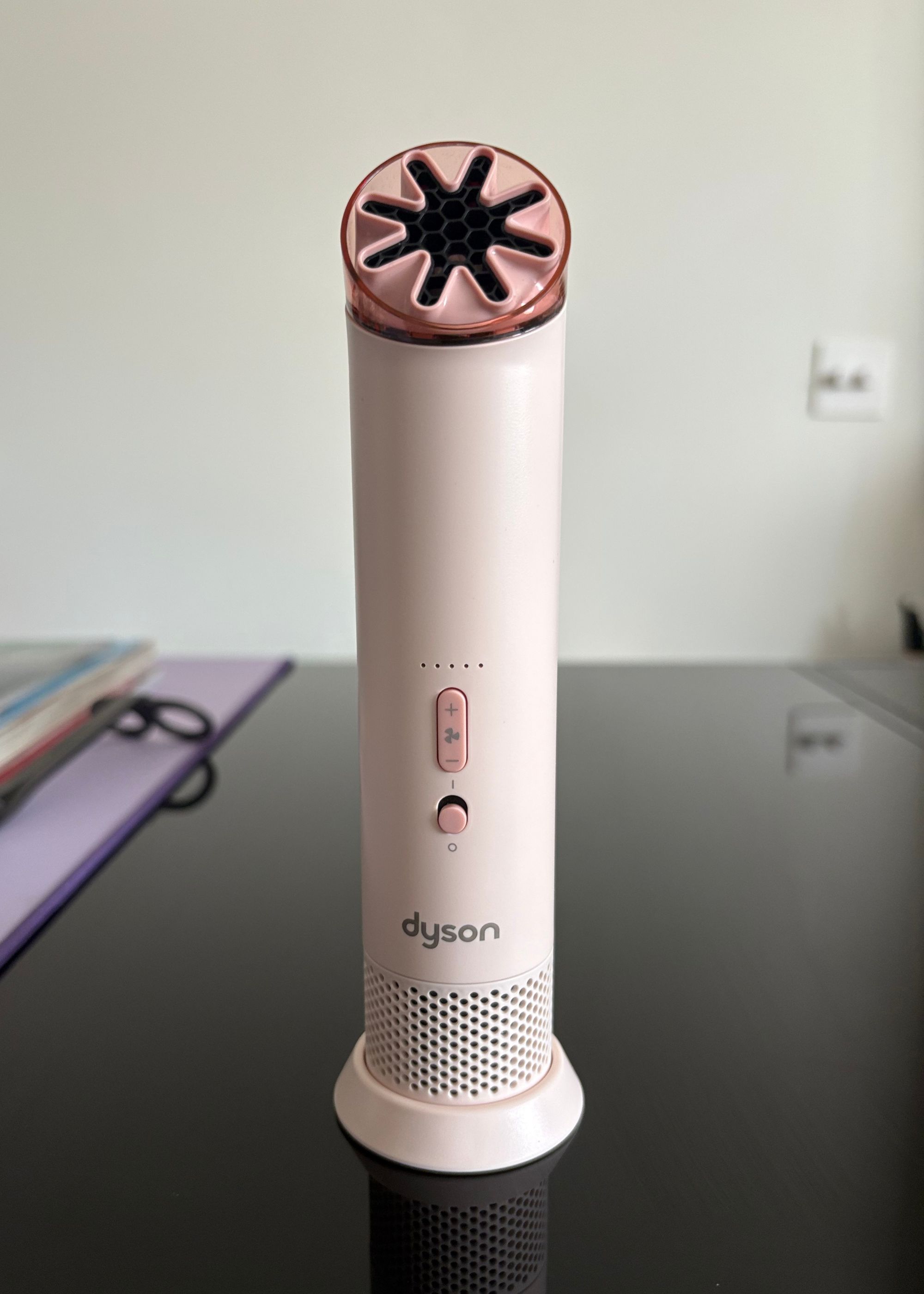 A blush Dyson portable mini fan on a stand on a glass coffee table