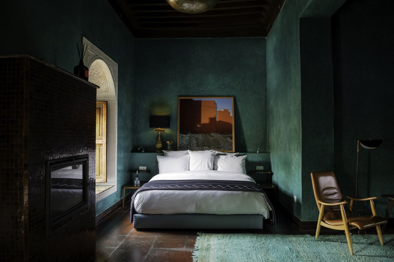 A green-painted hotel room filled with mid-century furniture and artworks.
