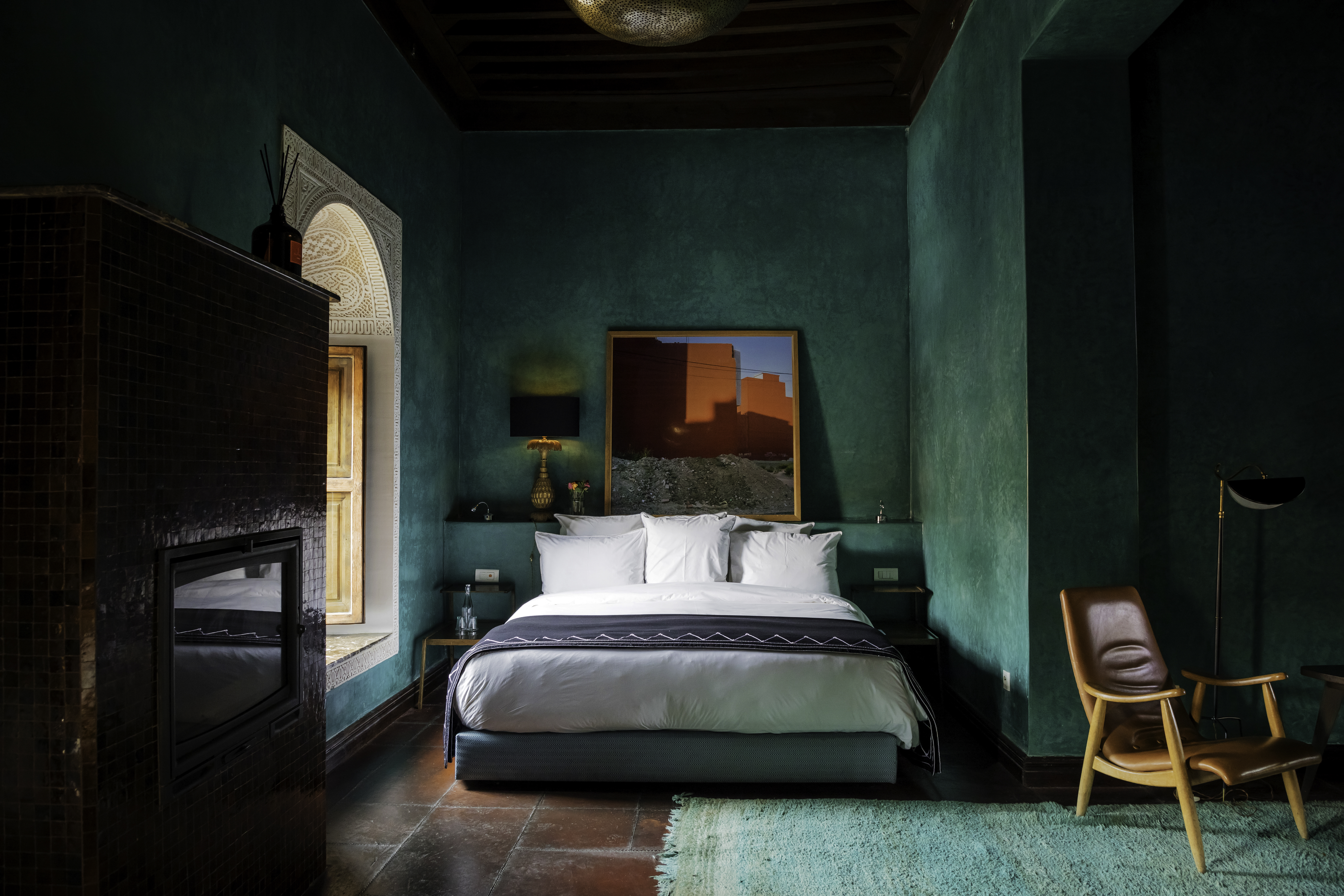 A green-painted hotel room filled with mid-century furniture and artworks.