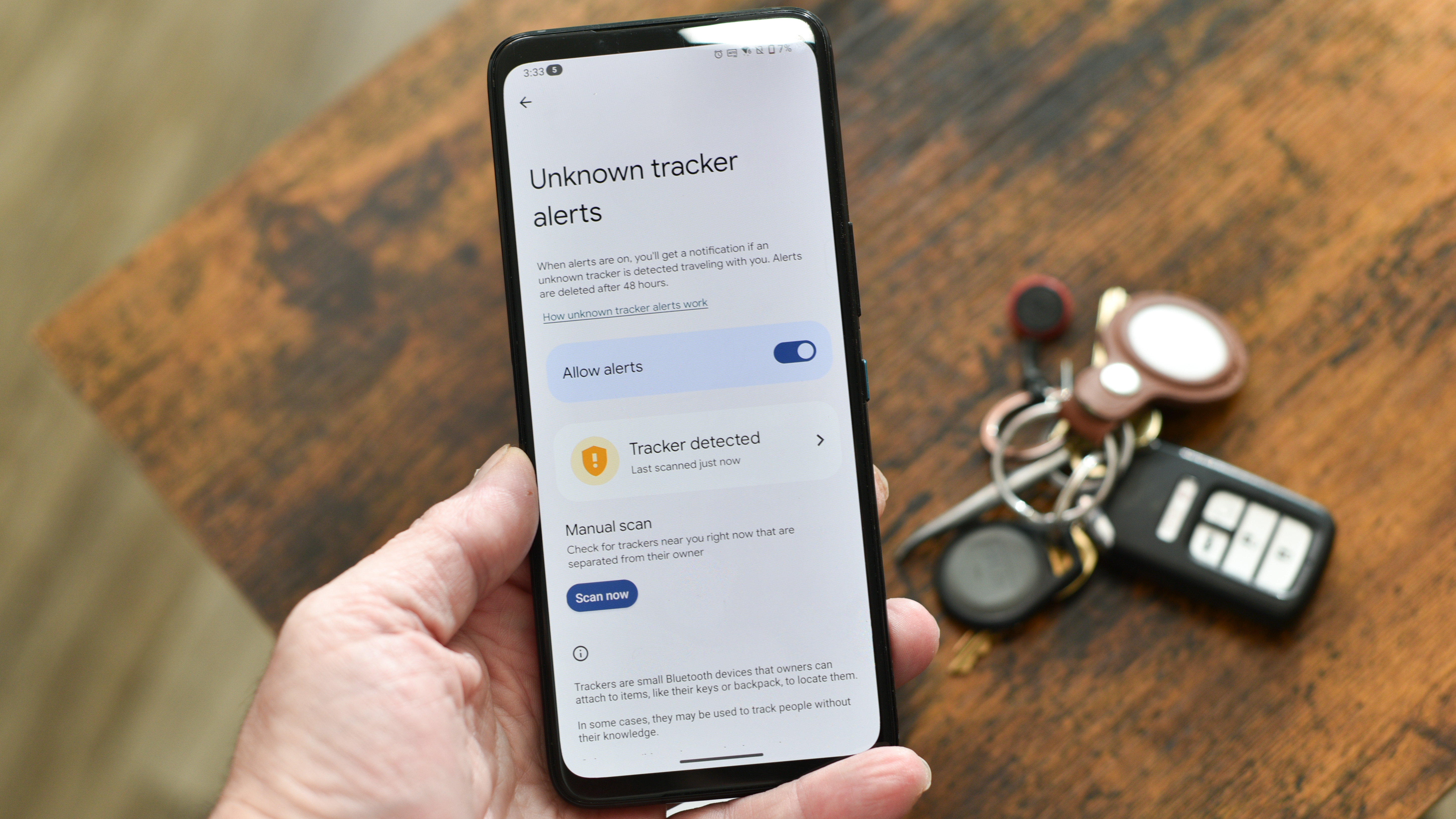 Unknown tracker alerts screen on an Asus phone with keychain and AirTag behind