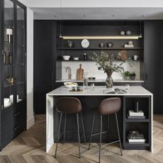black cabinets and shelving with a white kitchen island, brown bar stools and wooden flooring