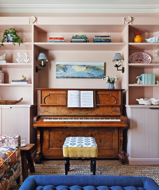 Music room with piano and inbuilt cabinet and two paterned sofas and pink walls