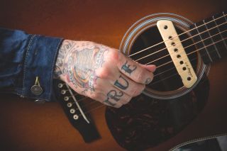 A hand strums an acoustic guitar