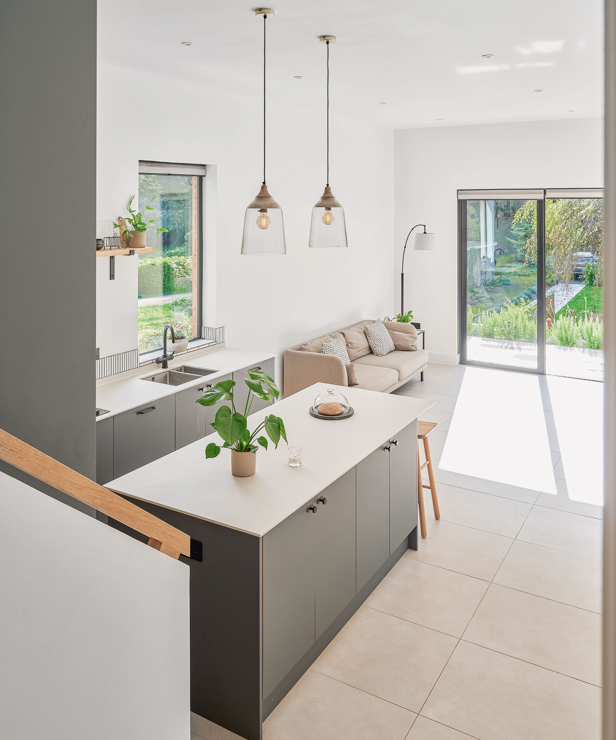 open-plan kitchen space with dark grey kitchen cabinets, large kitchen island, pendant lights overhead and a sofa in the background