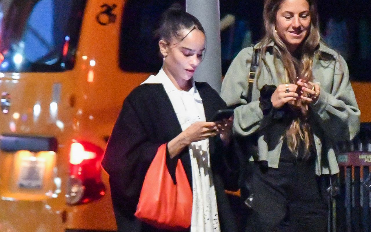 Zoe Kravitz wearing a black coat and carrying a red bag with her mary janes