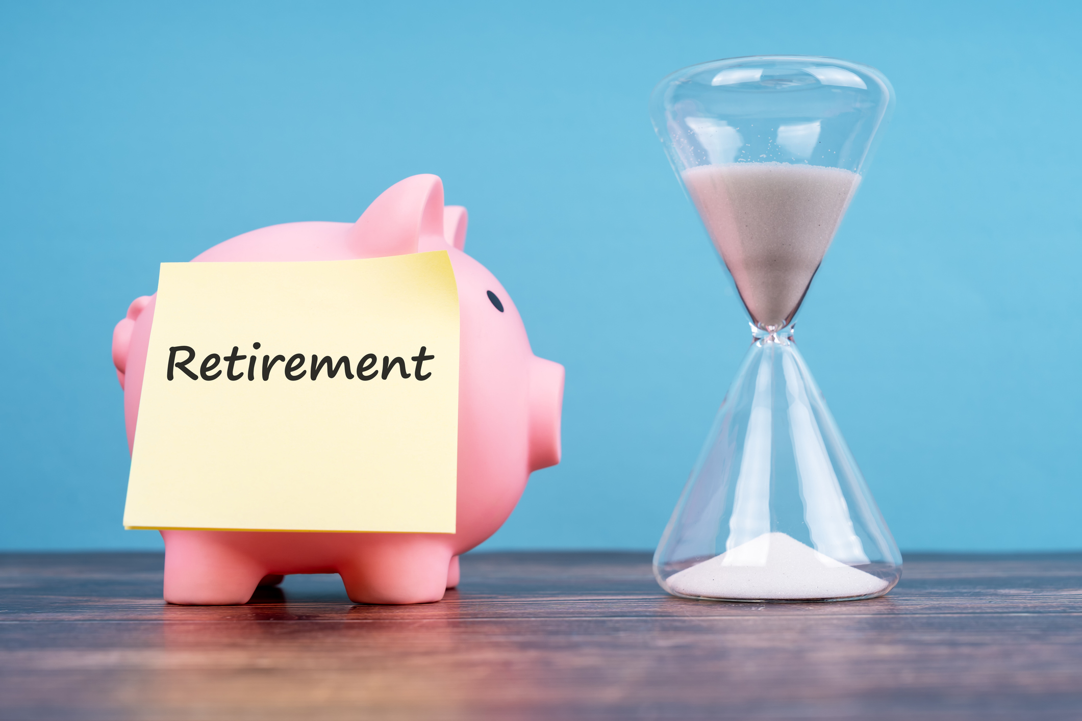 piggy bank with a note paper that says &#039;retirement&#039; beside an hourglass containing sand