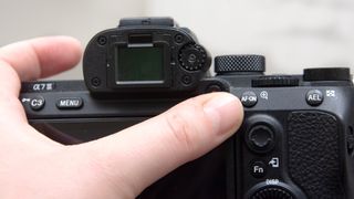 A thumb pointing towards the AF-ON button of a Sony A7 III camera