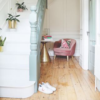 A hallway with hardwood floors and a white-painted staircase with potted houseplants decorating it