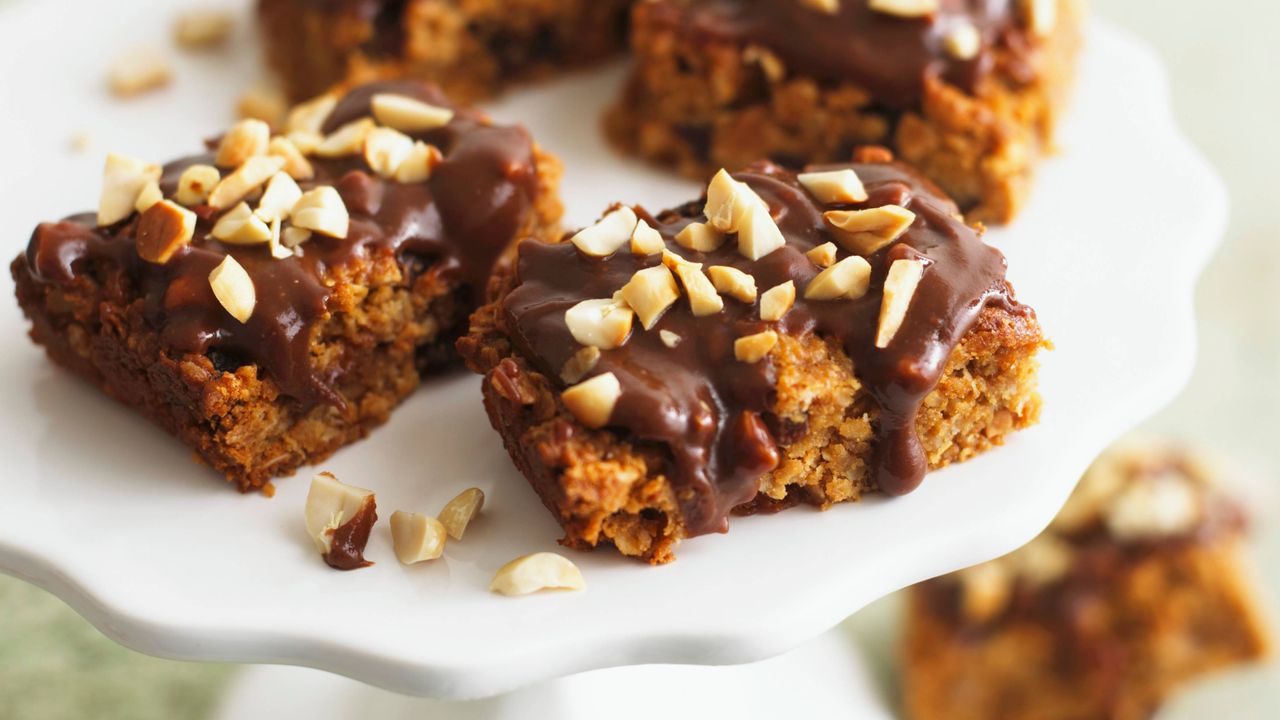 microwave flapjacks topped with melted chocolate and chopped nuts on a white cake stand