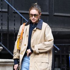 Gigi Hadid wearing a trench, polo top, light-wash jeans, and red Miu Miu loafers