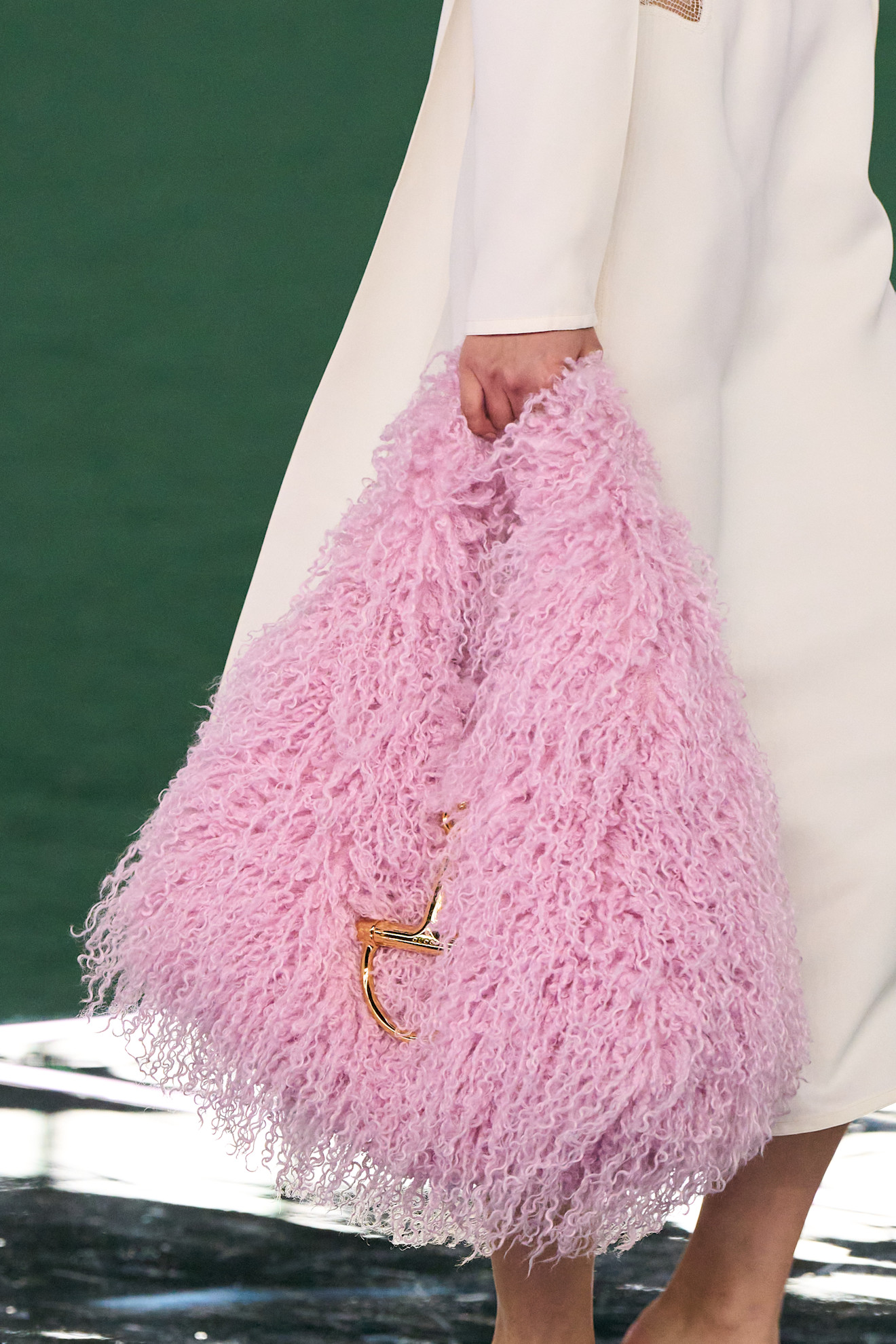 Fur accessory trend is shown in Gucci's fall-winter 2025 collection in a close photo of a model walking down the runway wearing a white coat with a shaggy pink hobo bag