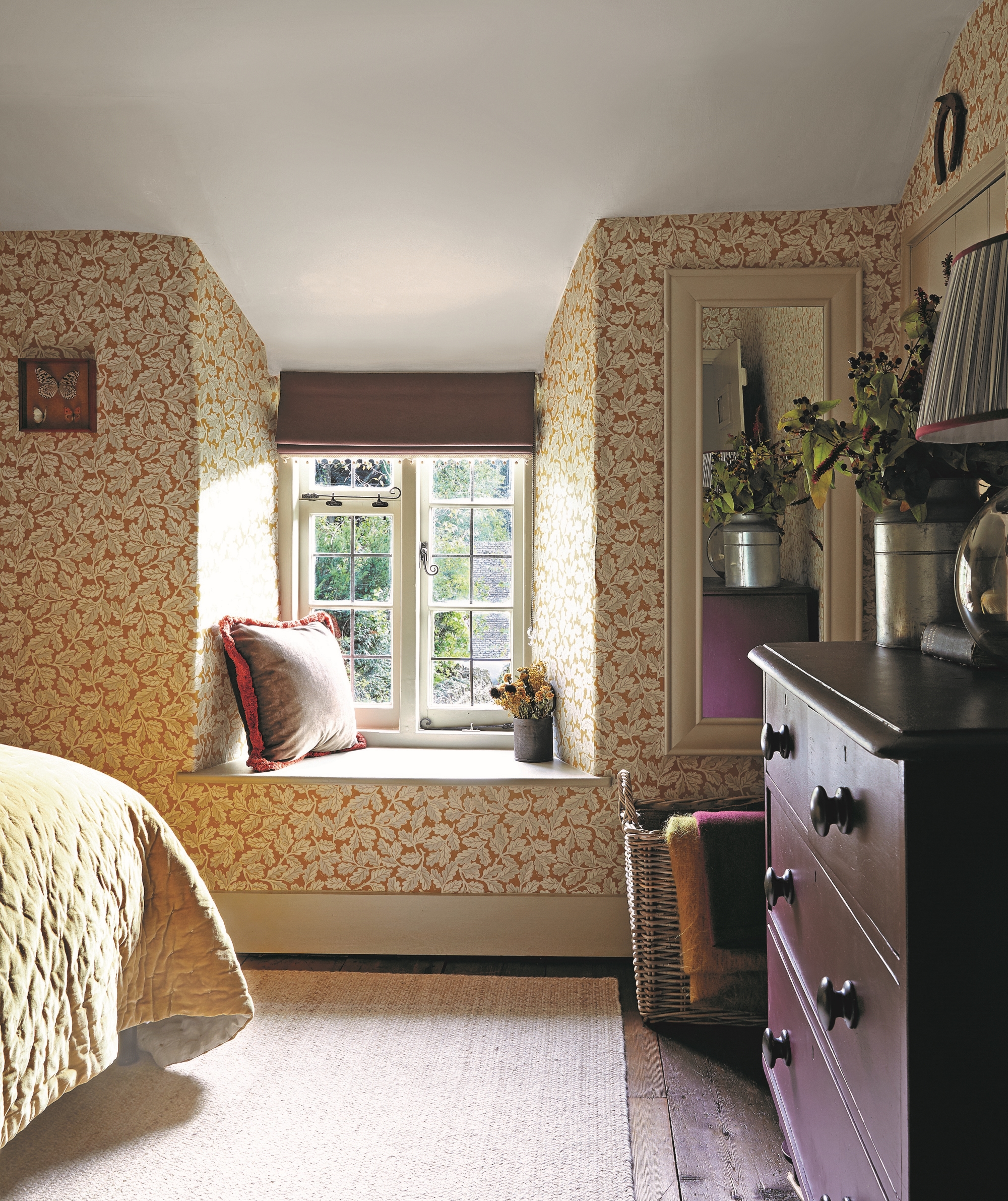 bedroom with yellow patterned wallpaper, bed with yellow throw, windowseat and maroon chest