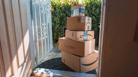 Amazon packages stacked on porch with screen and storm doors open