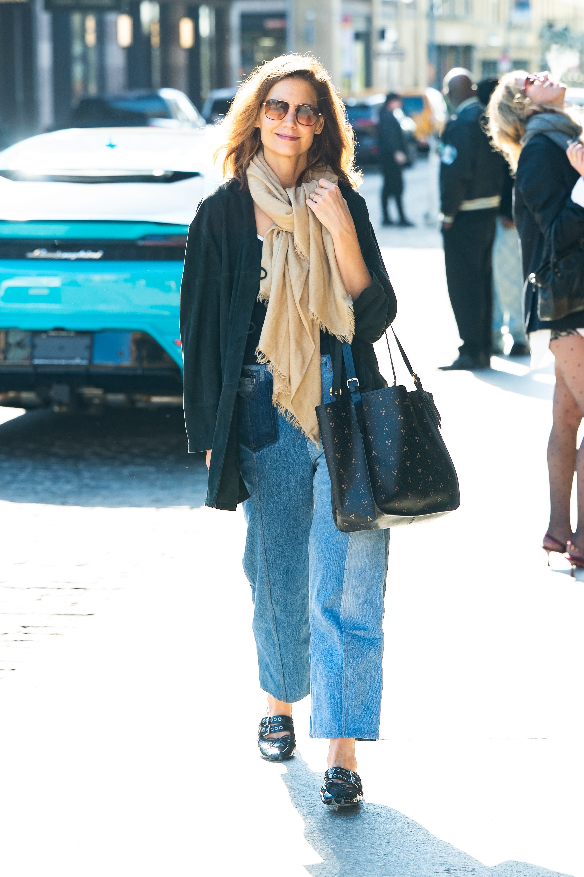 Katie Holmes walks down the street in New York wearing cropped jeans with black ballet flats, a black blazer and an oversized scarf.