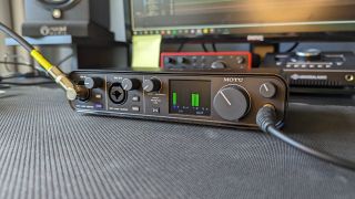 Angled shot of the Motu M4 audio interface on a desktop with interfaces and studio monitors in the background