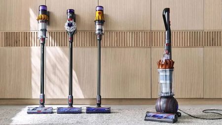 Four dyson vacuums against a light wooden wall on gray carpet