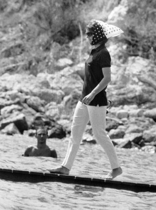 Black and white photograph of Jackie O walking on a pontoon