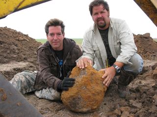 two men holding a large rock in a field